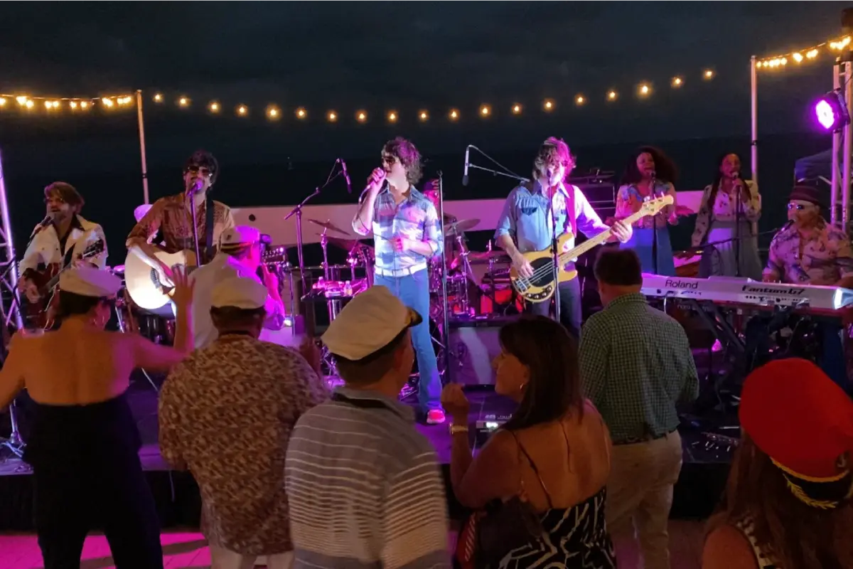 A live band performing on the sky deck under bistro string lighting for a night party cruise in Miami